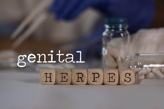 Words GENITAL HERPES composed of wooden dices. Pills, documents and a pen in the background.