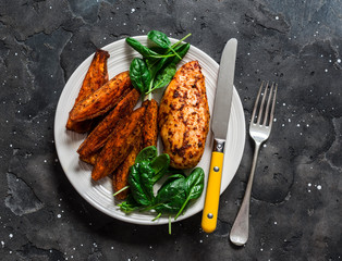 Baked chicken breast with sweet potatoes and spinach on a dark background, top view. Balanced...