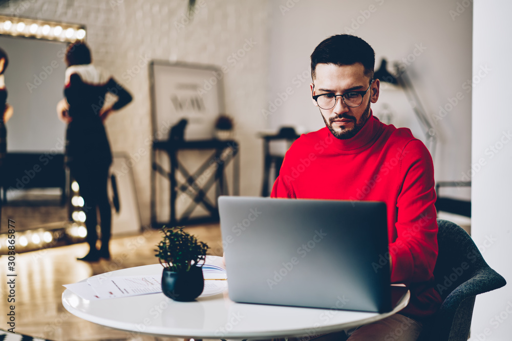 Poster concentrated young man in eyeglasses for vision correction watching tutorial on website via laptop c