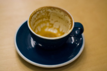 The ceramic blue cup is empty, with divorces from the cappuccino in coffee shop on wooden table. Morning drink.