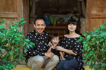 happy small asian family with daughter sitting in front door of a traditional country house