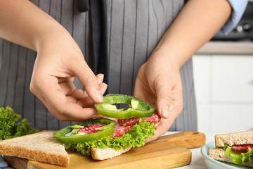 Woman making sandwich with green bell pepper and sausage at table, closeup