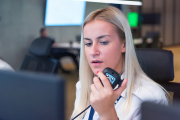 Female security guard operator talking on the phone, calling in the alarming event to the external...