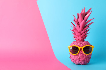Painted pink pineapple with sunglasses on two tone background, space for text