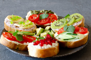 Open vegetarian sandwiches with vegetables, fruits and cream cheese on a gray background. Healthy breakfast concept. Copy space.