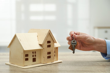 Real estate agent with house model and key at wooden table, closeup