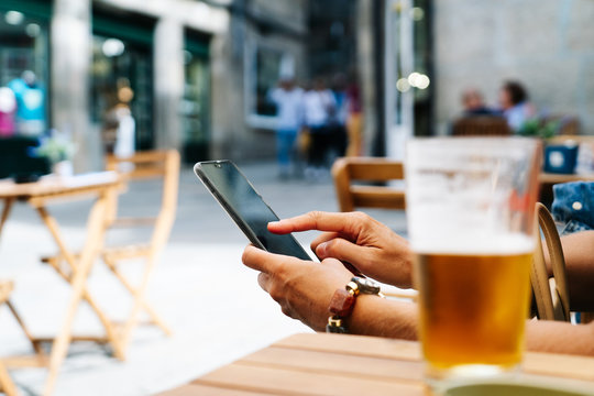 A woman's hand using the mobile phone on the terrace of a bar with a beer