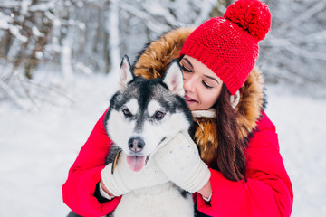 beautiful woman hugging her dog husky in winter park