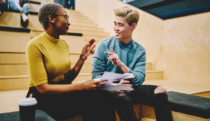 Positive multiracial colleagues gesture while discussing ideas and opinions about common project, smiling hipster male and female friends having communication on free time in college campus