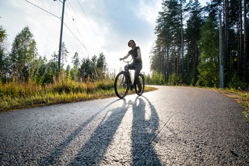 Happy woman rides a bike on a bicycle path near a pine forest. She is smiling and enjoying warm summer rain and the sun.