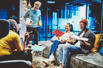Group of multicultural young people dressed in casual wear laughing during common work on startup project.Team of cheerful hipster students have brainstorming meeting in coworking space