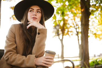 Portrait of attractive woman sitting on bench with coffee cup in autumn park