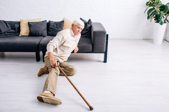 High Angle View Of Senior Man Holding Wooden Cane And Feeling Pain In Apartment