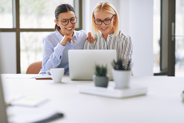 Two laughing businesswomen working on a laptop in an office