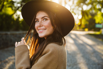 Image of attractive woman smiling while walking in green park outdoors