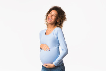 Excited african-american pregnant woman touching belly and laughing