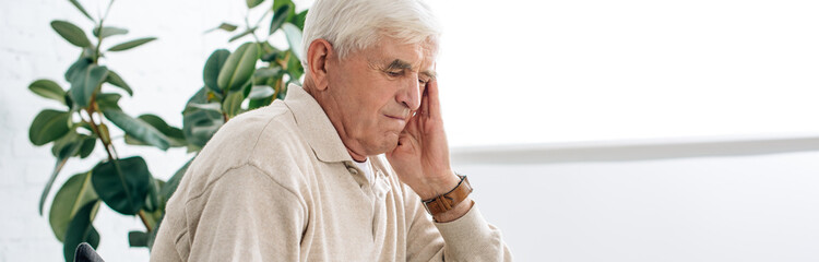 panoramic shot of senior man having headache in apartment