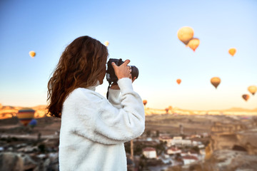 Travel photographer wearing white sweater taking a picture of balloons in Cappadocia. Travel...