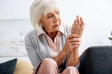 senior woman having hand pain and sitting on sofa in apartment
