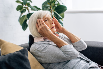 senior woman having headache and sitting on sofa in apartment