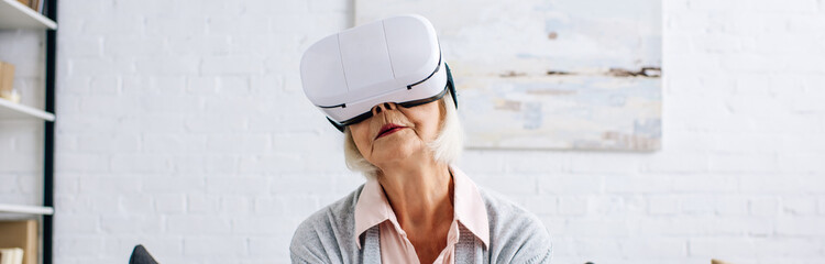 panoramic shot of senior woman with virtual reality headset in apartment - Powered by Adobe