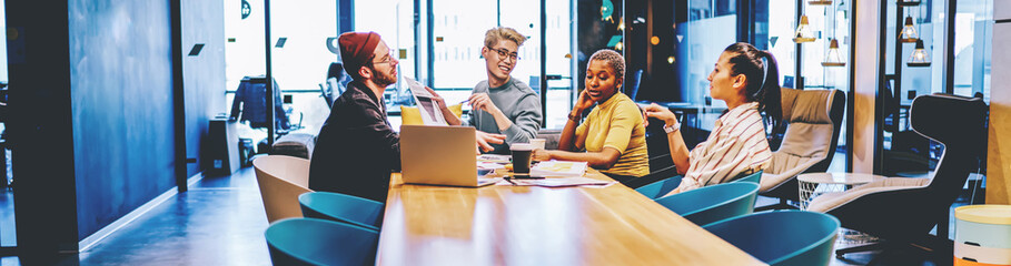 Positive multiracial crew of employees having brainstorming session cooperate  at modern interior office, positive male and female colleagues discussing creative solution for startup project.