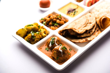 Indian vegetarian Food Thali or Parcel food-tray with compartments in which Malai Kofta, chole, Dal tarka, dry aloo sabji, chapati and rice with sweet gulab jamun served - obrazy, fototapety, plakaty