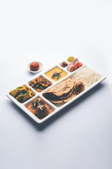 Indian vegetarian Food Thali or Parcel food-tray with compartments in which Malai Kofta, chole, Dal tarka, dry aloo sabji, chapati and rice with sweet gulab jamun served