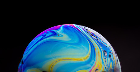 close up of a colorful soap bubble isolated on a black background, looking like a planet in space. - obrazy, fototapety, plakaty