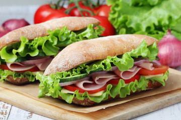 Two sandwiches with fresh vegetables, ham and cheese in ciabatta bread - obrazy, fototapety, plakaty
