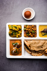 Indian vegetarian Food Thali or Parcel food-tray with compartments in which Malai Kofta, chole, Dal tarka, dry aloo sabji, chapati and rice with sweet gulab jamun served