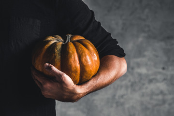 Man holding ripe pumpkin in hands on a gray background