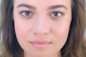 Portrait of beautiful young girl after beauty procedure of permanent eyeliner in cosmetology clinic. Face closeup view. Woman is looking at camera on white background, front view.