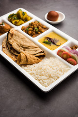 Indian vegetarian Food Thali or Parcel food-tray with compartments in which Malai Kofta, chole, Dal tarka, dry aloo sabji, chapati and rice with sweet gulab jamun served