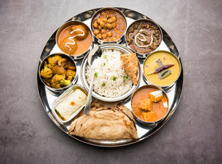 Indian vegetarian Food Thali or platter includes paneer butter masala, dal makhani / tarka, chole papad, kofta curry, gulab jamun, aloo-gobi sabji, chapati and rice with Bengali sweet served