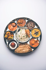Indian vegetarian Food Thali or platter includes paneer butter masala, dal makhani / tarka, chole papad, kofta curry, gulab jamun, aloo-gobi sabji, chapati and rice with Bengali sweet served