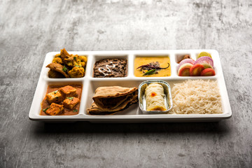 Indian vegaterian Food Thali or Parcel food-tray with compartments in which paneer, dal makhani / parka, aloo-gobi sabji, chapati and rice with Bengali sweet served