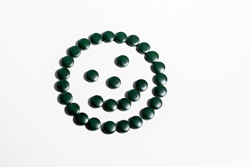 Spirulina tablets on a white background in the form of a smile.