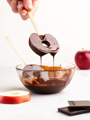 Delicious fresh Red Apple slices in melted chocolate with pieces of chocolate, White background, photo of cooking process, healthy dessert. 