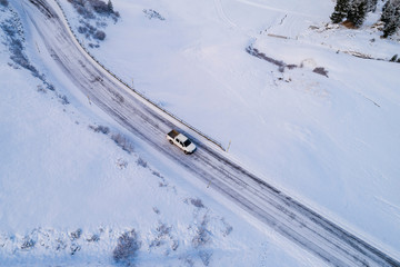 white car and road from above in the Italian Alps in South Tyrol, during winter / Sunny winter day with harsh shadows and lot of snow