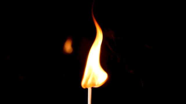 Red safety match igniting and burning out against a black background. Locked close up shot