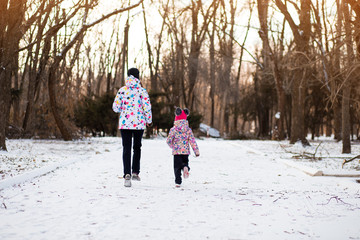 Fototapeta na wymiar Mother and little girl in colored jackets jogging by snow in winter park. Concept of instill sports health habits in children