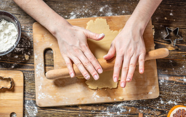 Woman rolls out the dough with a rolling pin and shapes festive gingerbread. Christmas time cooking delicious cookies.