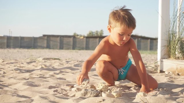 small blond boy plays with the sand on a pristine beach.