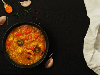 Vegetarian and vegan yellow pea soup with carrots, paprika and turmeric. Soup on a black stone background, next to cloves of garlic, sprigs of rosemary and turmeric. Flat lay. Natural lighting.