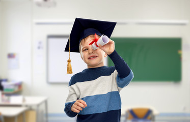 school, education and learning concept - happy little boy in bachelor hat or mortarboard looking...