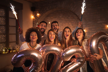 Friends celebrating New Years Eve waving with sparklers and holding 2020 balloons