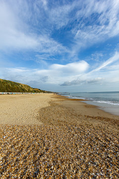 A view of the Boscombe Beach with sandy beach, colorful beach huts along the promenade with cliff under a beautiful blue sky and some whites clouds