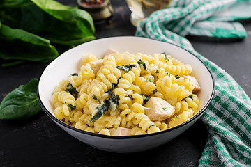 Fusilli pasta with a creamy sauce with chicken meat, parmesan cheese and spinach on a bowl on a dark background.