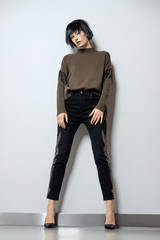 Fashion model in black wig, pullover with fringe and jeans with rhinestones